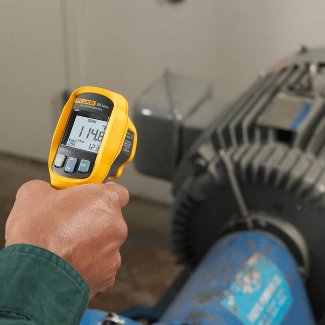 A mechanical engineer performing predictive maintenance by using the FLUKE 62 Max+ infrared thermometer to check the front bearing temperature of an industrial induction motor, displaying 114.8°F with a maximum value of 123°F to prevent overheating and motor failure.