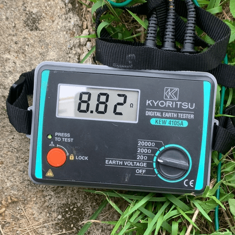 The KYORITSU KEW 4105A portable earth tester is in use outdoors, displaying a ground resistance measurement of 8.82 ohms with its shoulder strap attached.