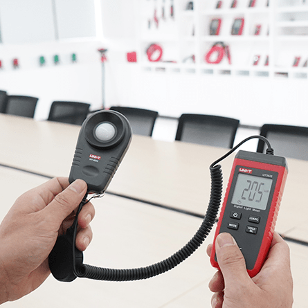 A technician using the UNI-T UT383S lux meter to perform a workplace lighting audit, with the device showing a 205 Lux reading in a meeting room.