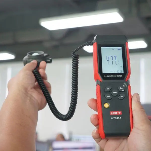 Technician uses UNI-T UT381A meter with detached probe in hand to check factory lighting, displaying an illuminated 477.1 Lux reading.