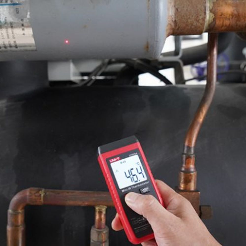 Mechanic using UNI-T UT306A automotive infrared thermometer to diagnose overheating on a truck exhaust pipe silencer, showing 46.4°C precision reading
