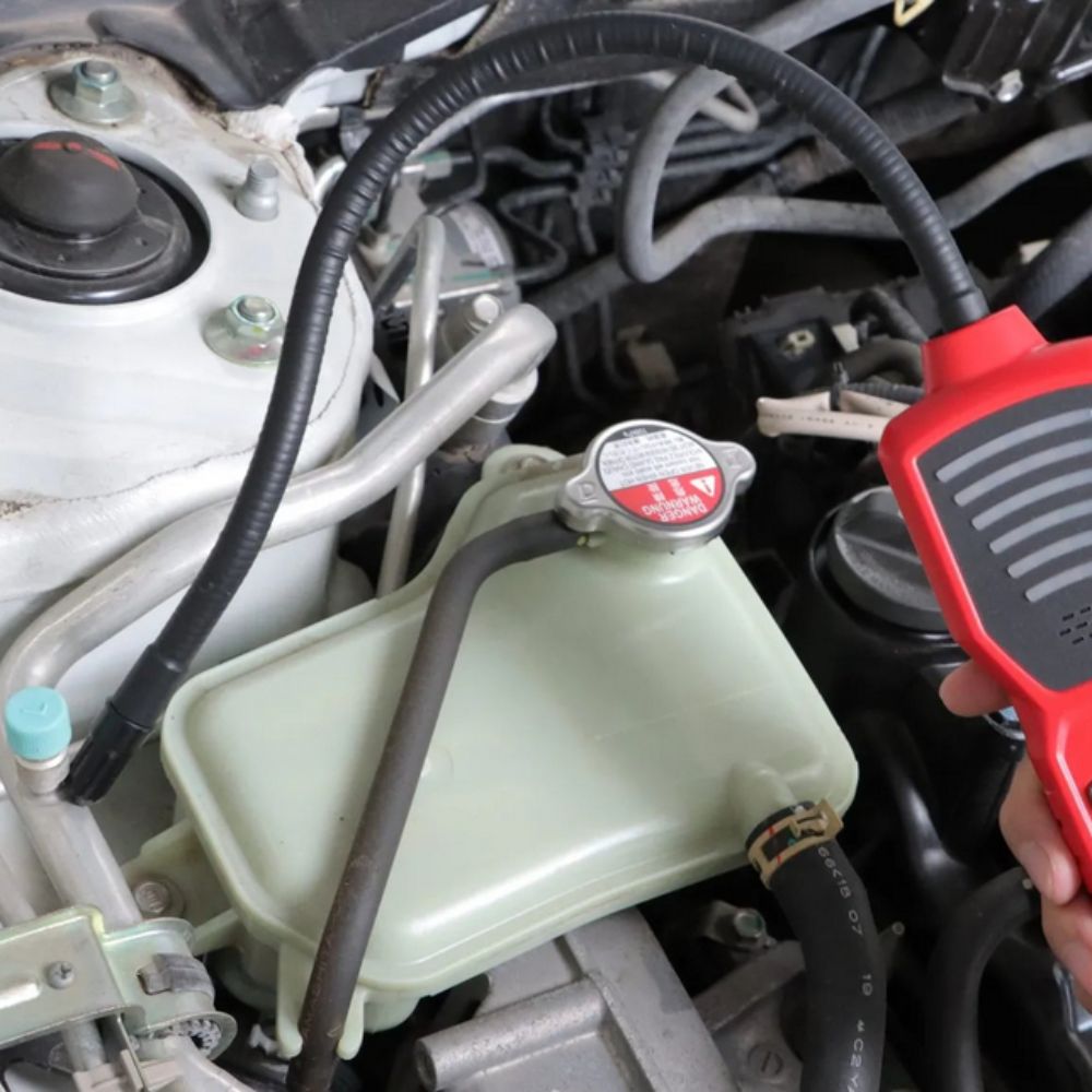 Checking for R134a cooling gas breaches with the UT336B automotive freon leak detector along a car AC compressor pipeline.