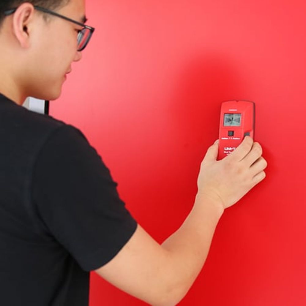 Using the UNI-T UT387A wall stud scanner on drywall to safely detect hidden wooden studs before drilling.