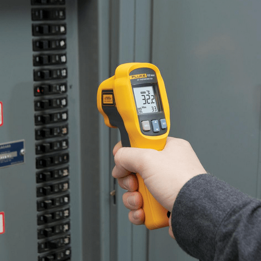 A technician using the FLUKE 62 Max+ handheld laser thermometer to perform electrical safety inspection on an industrial control panel, measuring 32.2°C surface temperature with a maximum reading of 33°C to detect hotspots and prevent circuit breaker failure.