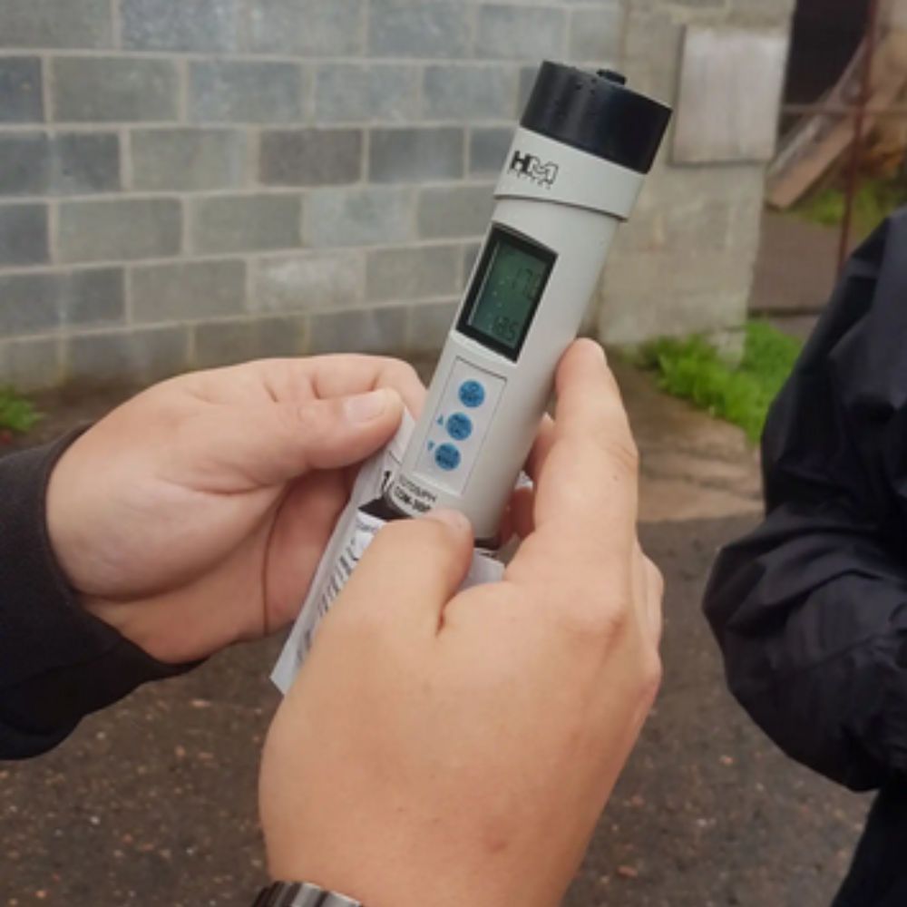 Scientist holding HM Digital COM-300 multi-parameter pH EC TDS temperature meter while carefully testing a liquid sample, waterproof combo pen for laboratory water quality, RO system and wastewater analysis