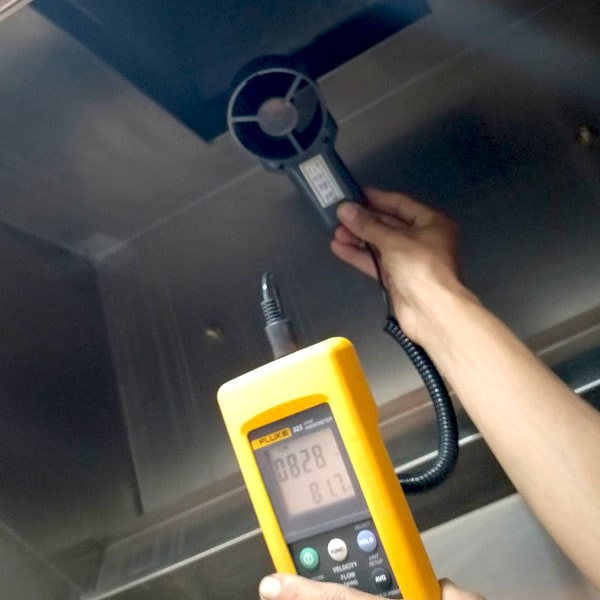 An HVAC technician using the FLUKE 925 anemometer to measure airflow from an overhead ventilation grill, ensuring proper system performance.