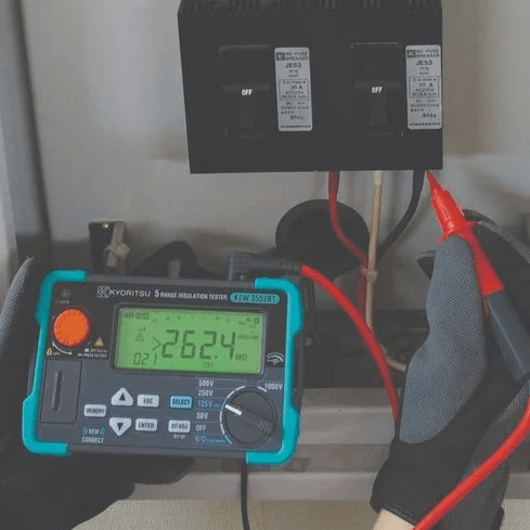 Technician testing an electrical panel with KYORITSU KEW 3552BT insulation tester, displaying 262.4 MΩ, backlight off, 125V range.