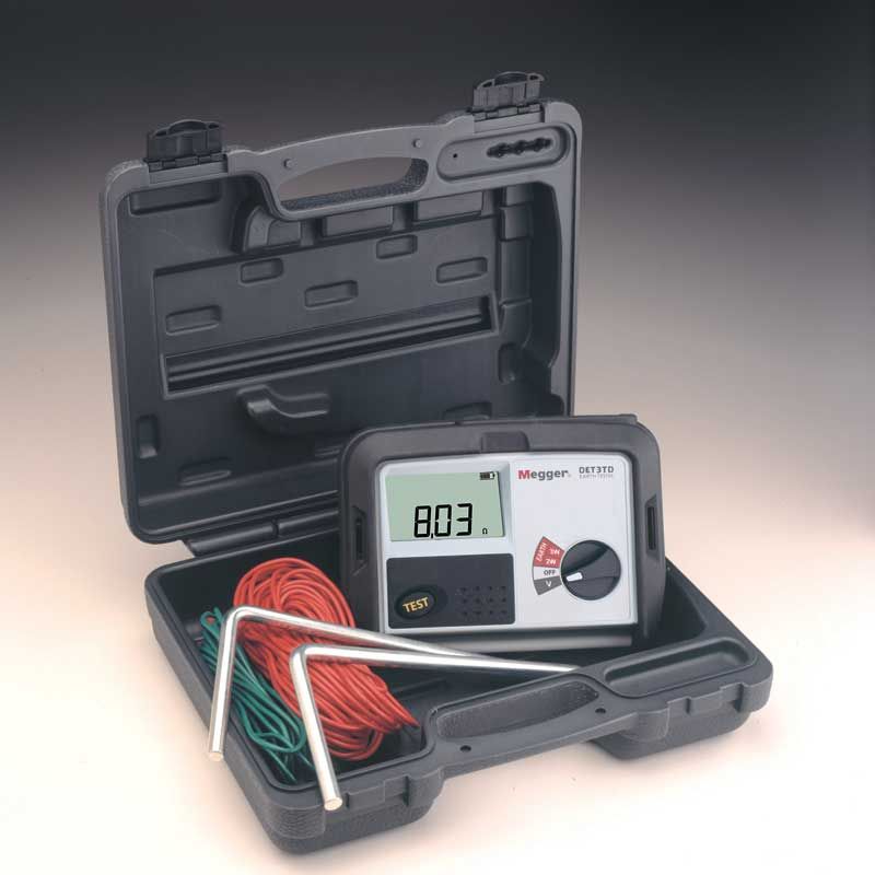 The MEGGER DET3TD earth testing kit in its hard case, showing the tester with a reading of 8.03 ohms alongside its neatly arranged spikes and wire spools.