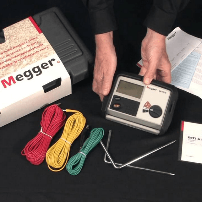 The MEGGER DET3TD earth tester shown with its complete accessory set, including auxiliary earth spikes, color-coded wire spools, and the protective hard case.