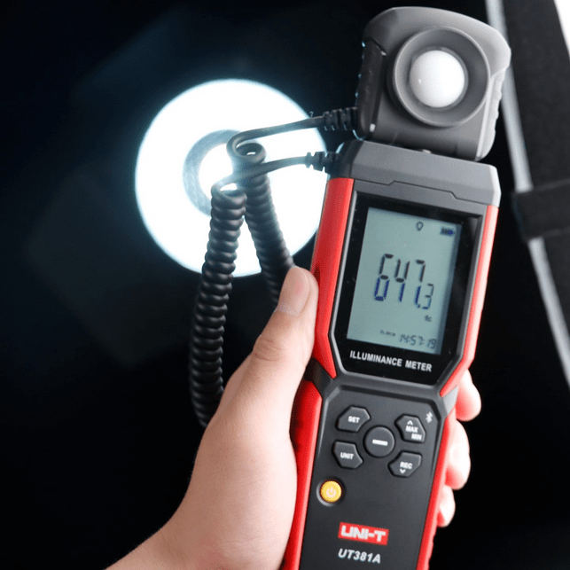 A photographer uses the UNI-T UT381A lux meter with mounted detachable probe to measure studio lighting, showing 647.3 Lux.