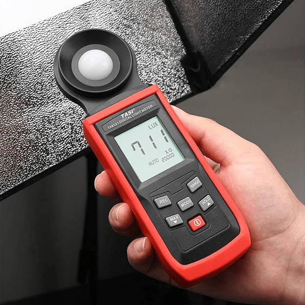 A photographer using the TASI TA8121 light meter to measure and adjust studio lighting levels, with a 711 Lux reading shown.
