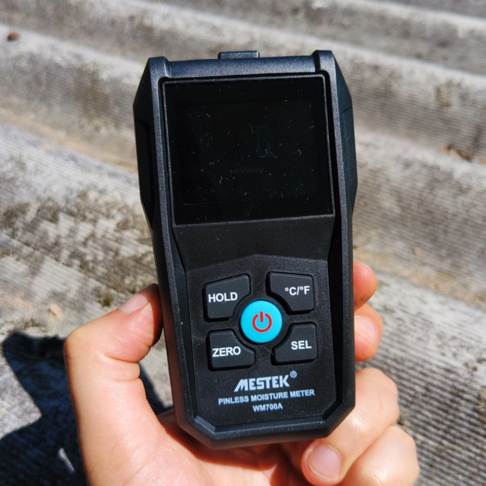 Mestek WM700A handheld hygrometer checking moisture levels on roofing sheets to identify leaks in sunny outdoor conditions.