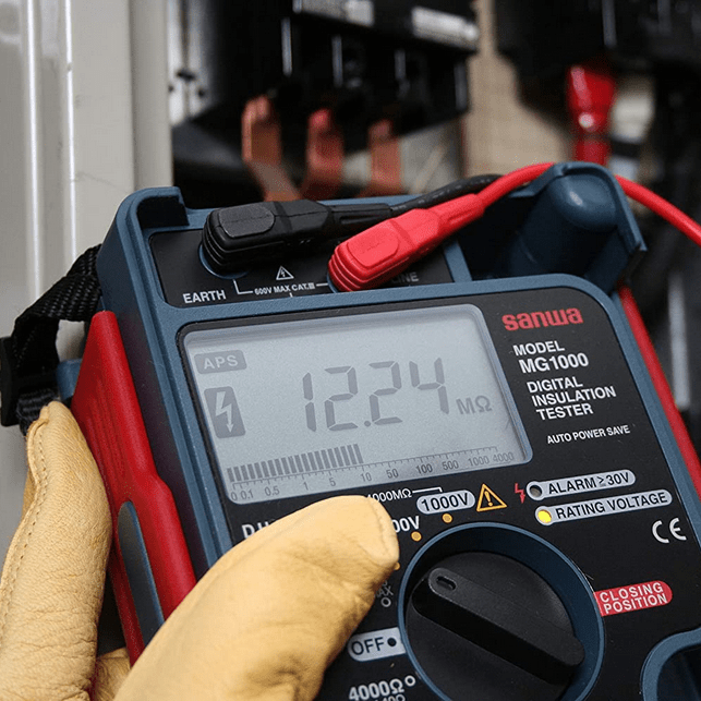 Electrician measuring electrical panel insulation with SANWA MG1000 insulation tester displaying 12.24 megaohms on 250V range