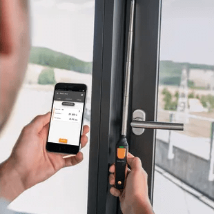 A technician using the testo 405i thermal anemometer to measure air velocity and detect drafts near an interior doorway.