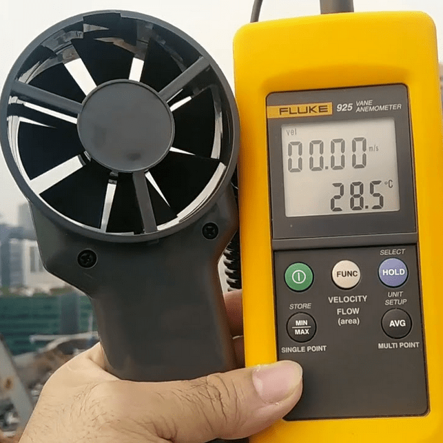 A technician preparing to measure outdoor wind speed with the FLUKE 925 digital anemometer on the rooftop of a building.