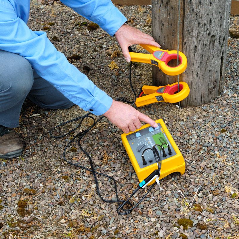 A technician performing a ground resistance test on gravel soil using the FLUKE 1625-2, with test leads connected for measurement.