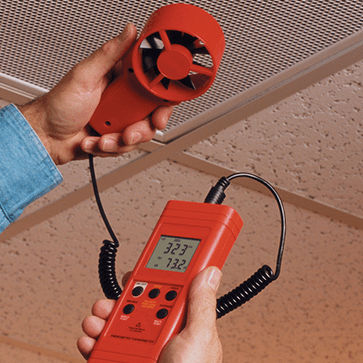A technician uses the AMPROBE TMA10A air flow meter with its vane probe to accurately measure air velocity from an overhead HVAC vent for system balancing.