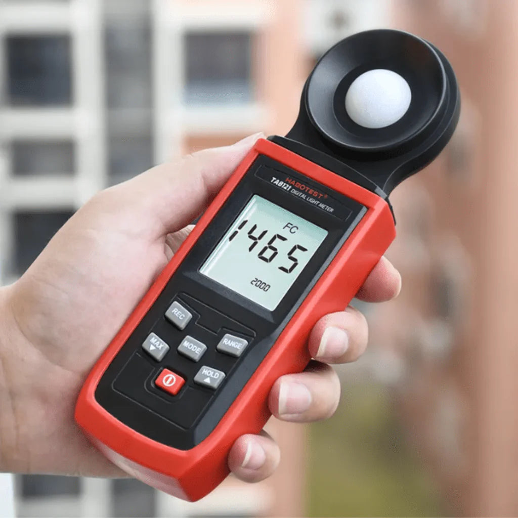 A technician holding the TASI TA8121 portable lux meter to measure bright outdoor sunlight, showing a reading of 1465 FC (Foot-candles).