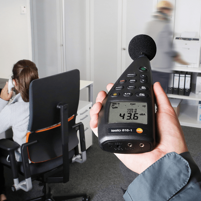 A technician uses the TESTO 816-1 handheld decibel meter to perform a workplace noise assessment in a quiet office, showing a reading of 43.6 dBA for occupational health monitoring.
