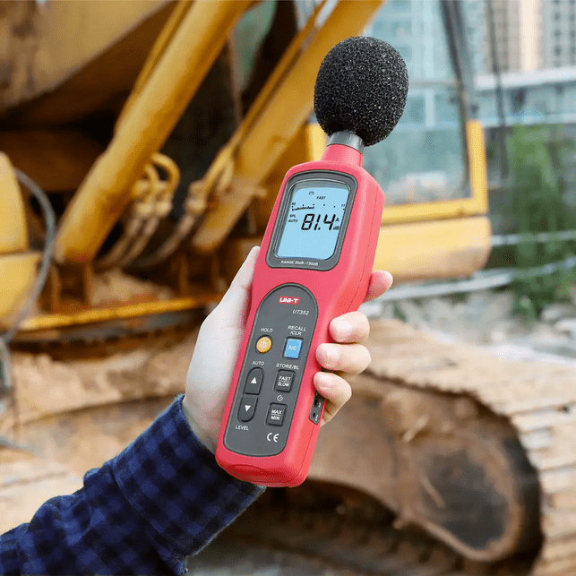 A technician using the UNI-T UT352 sound meter to perform industrial noise measurement on heavy machinery, ensuring workplace safety and OSHA compliance.