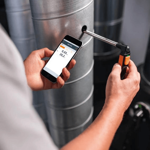 A technician performing an in-duct airflow measurement by inserting the flexible, telescopic probe of the testo 405i anemometer into a cylindrical ventilation duct.