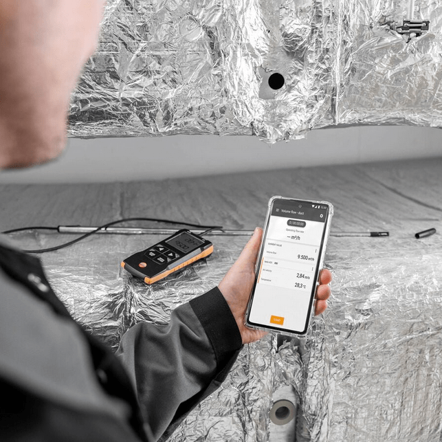 Live data from the TESTO 425 anemometer is displayed on a smartphone via the Testo Smart App, showcasing its wireless data logger and reporting capabilities.