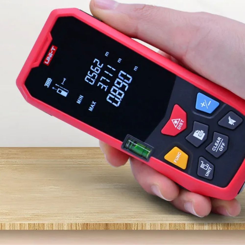 UNI-T LM100A digital laser distance meter being used to measure room dimensions on a construction site