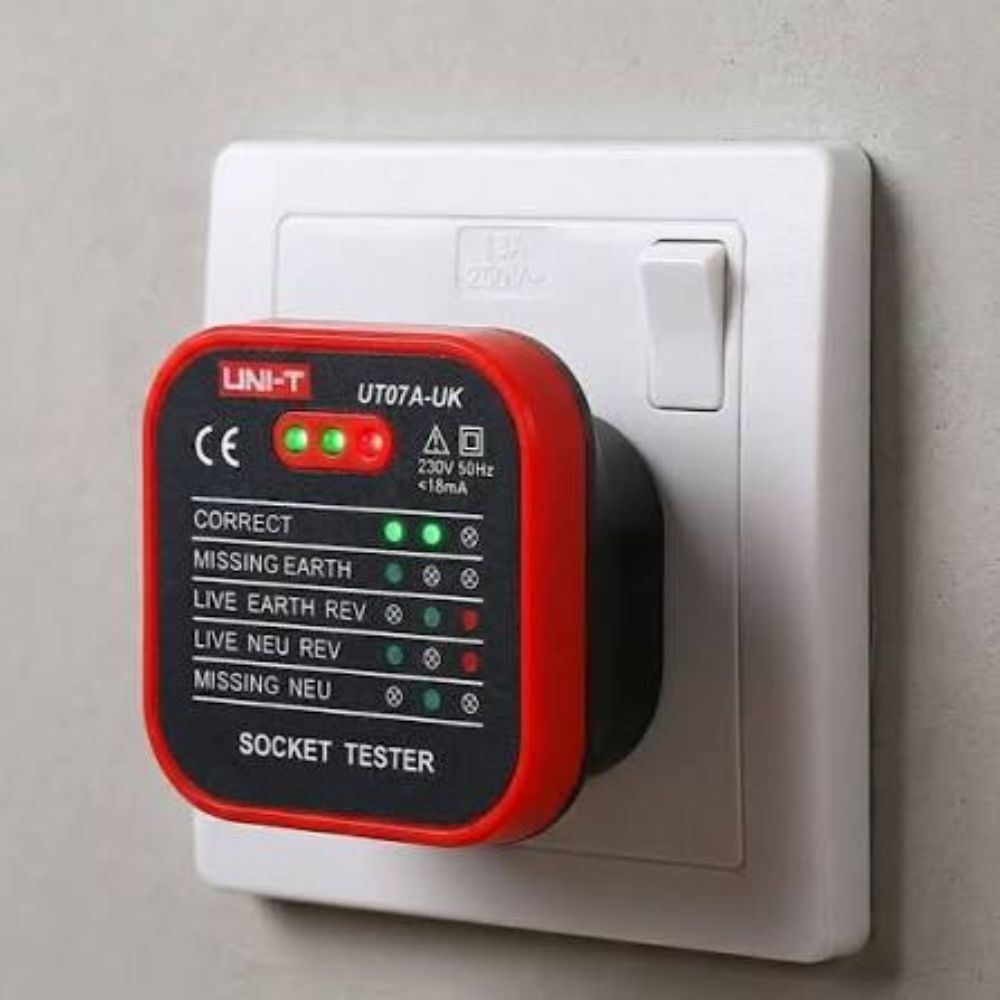 UNI-T UT07A-UK 13A socket tester plugged into a UK-style 230V wall outlet with LED indicators lit for wiring check