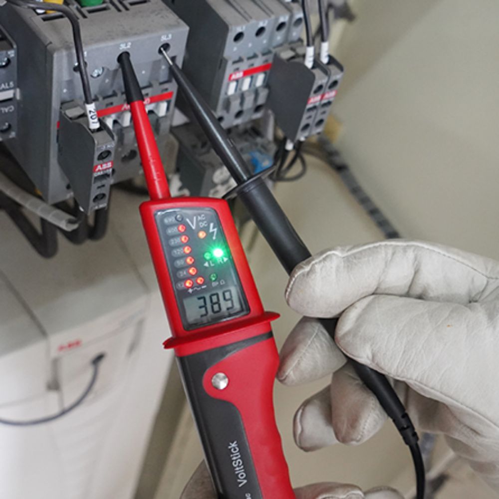 Electrician using the UNI-T UT15C continuity tester to safely check phase rotation and voltage levels on an industrial 3-phase power supply.