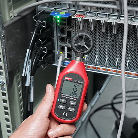 IT technician measures cooling fan performance in a network server rack with the UNI-T UT363BT, confirming an airflow of 1.5 m/s for system diagnostics.