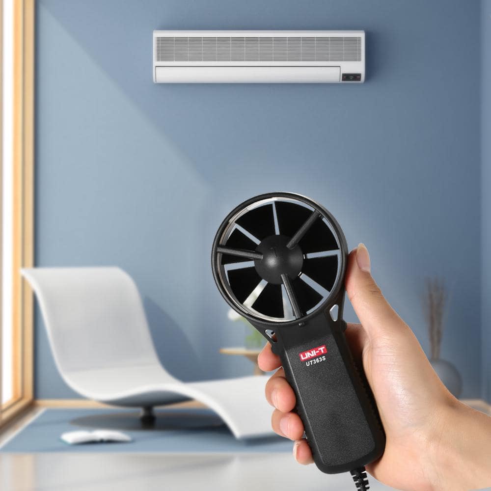 Close-up of the UNI-T UT363S anemometer's split-vane sensor held up towards an air conditioner indoor unit, demonstrating its use for HVAC air flow measurement.