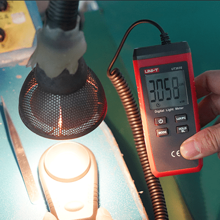 The UNI-T UT383S light meter's probe measuring a strong light source, with the digital display showing a reading of 3058 Lux.
