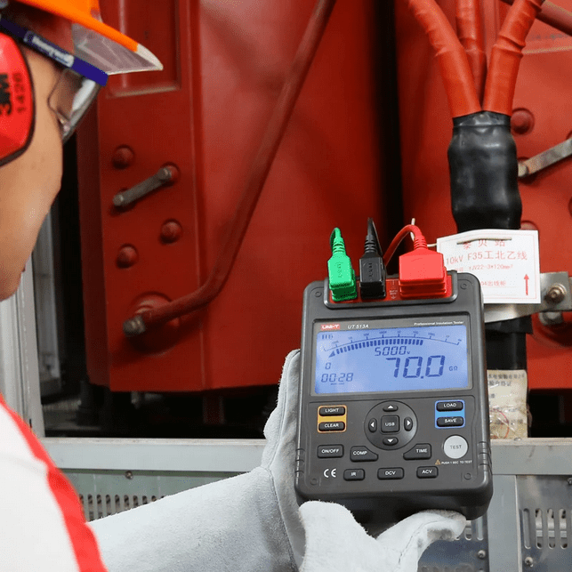 Technician using UNI-T UT513A digital insulation tester to check large transformer insulation resistance, displaying 70 gigaohm reading in professional electrical maintenance