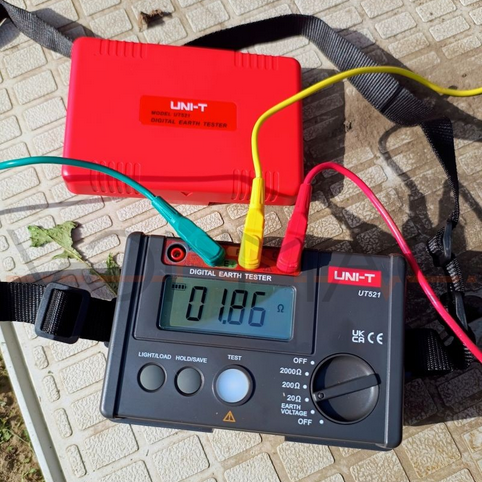 A UNI-T UT521 earth tester performing a 3-wire ground resistance measurement, displaying a reading of 1.86 ohms while connected to earth spikes.