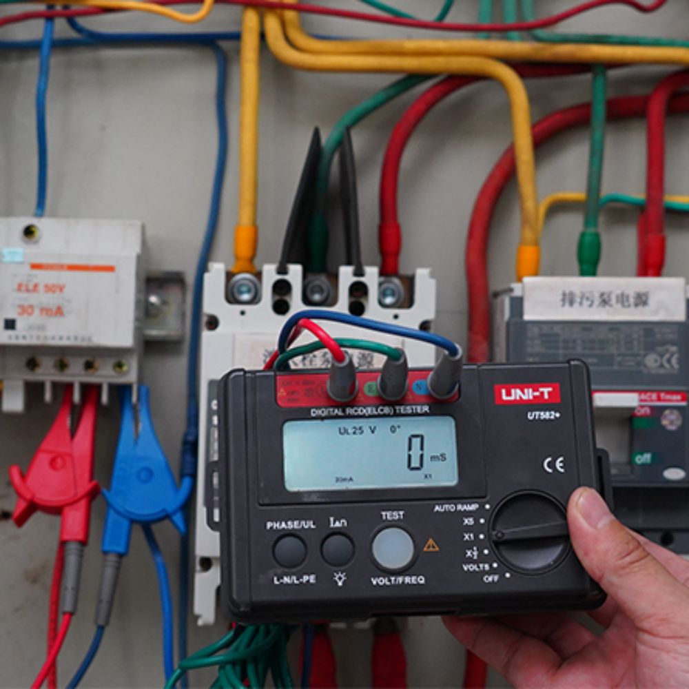 UNI-T UT582+ RCD tester performing trip time test on a large industrial electrical panel board
