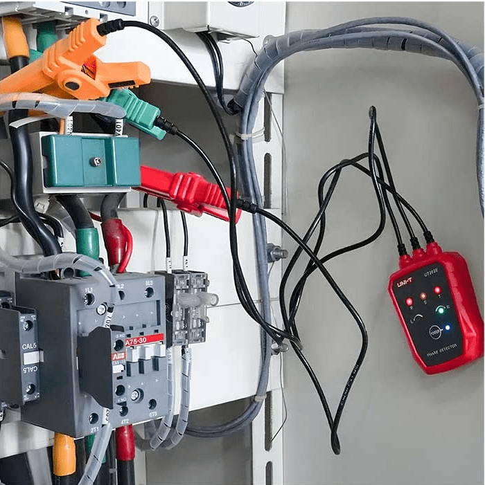 The UNI-T UT262E phase rotation tester mounted inside a motor power supply panel, with LED phase-sequence indicators clearly lit.