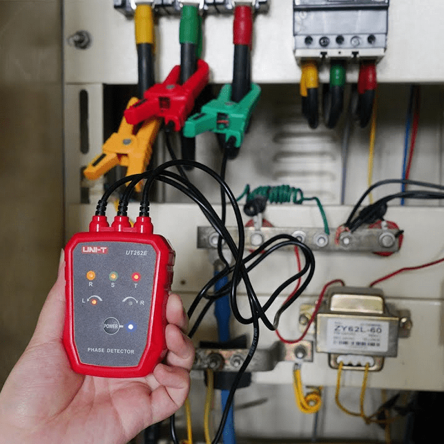 A technician uses the UNI-T UT262E phase rotation tester with three leads connected to motor control panel supply wires, LED phase-sequence indicators visible.